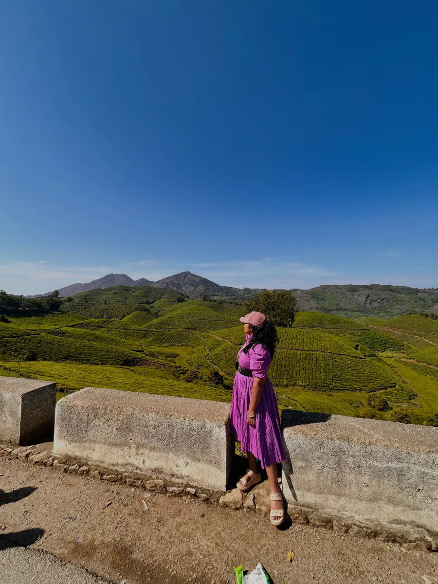 Reena in a purple dress at a viewpoint above the tea hills of Munnar