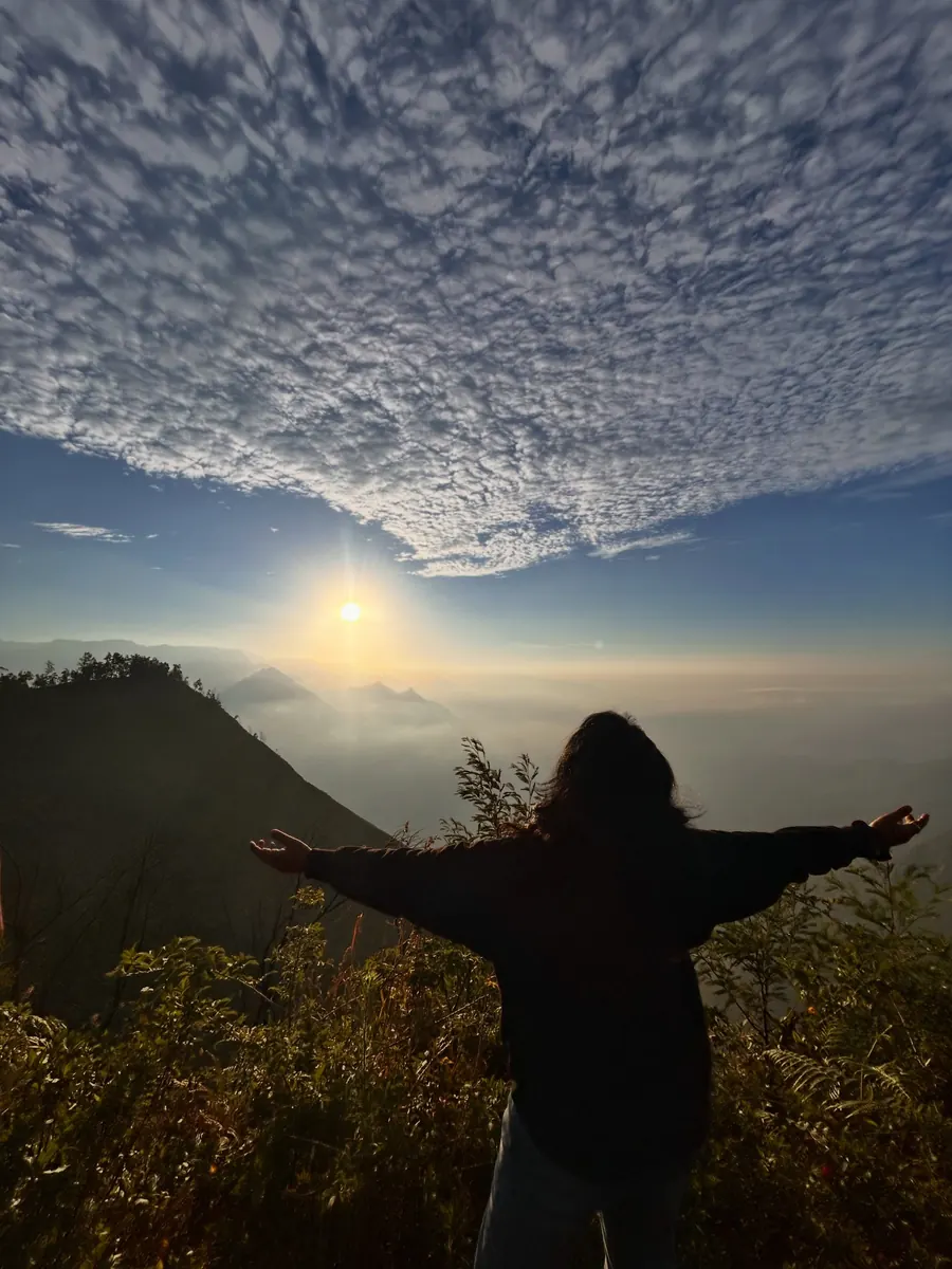 Reena with her arms open to the sunrise above a sea of clouds